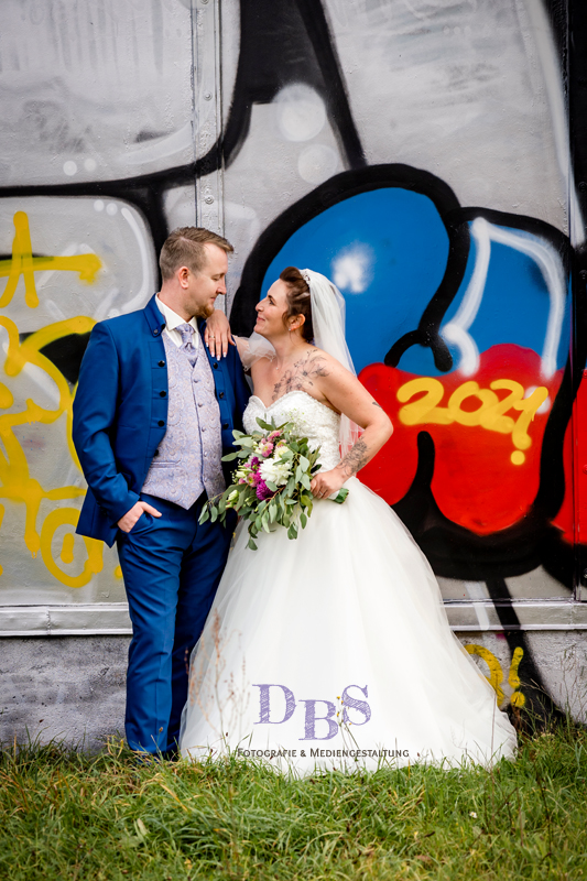 Hochzeitspaar an einer Grafitti Wand schauen sich verliebt an